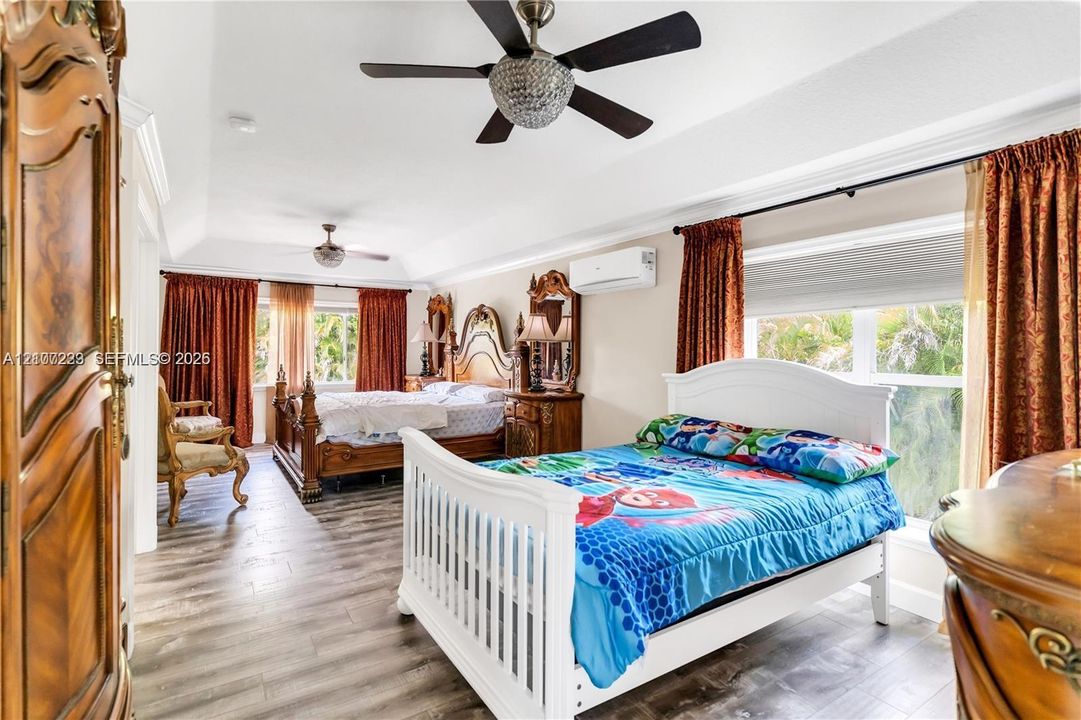 Tray ceiling with recessed lighting, wood-finish flooring, dual ceiling fans with crystal accents, and wall-mounted ductless climate control unit