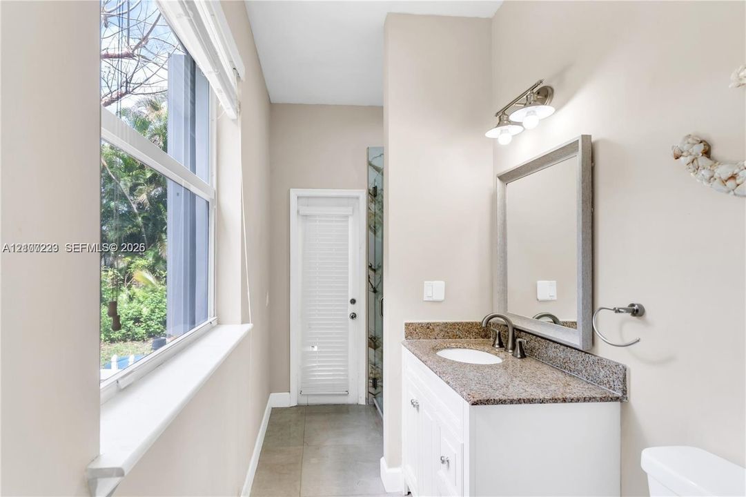 Bathroom featuring a white vanity with a stone countertop, an oval undermount sink, a framed mirror, and tile flooring