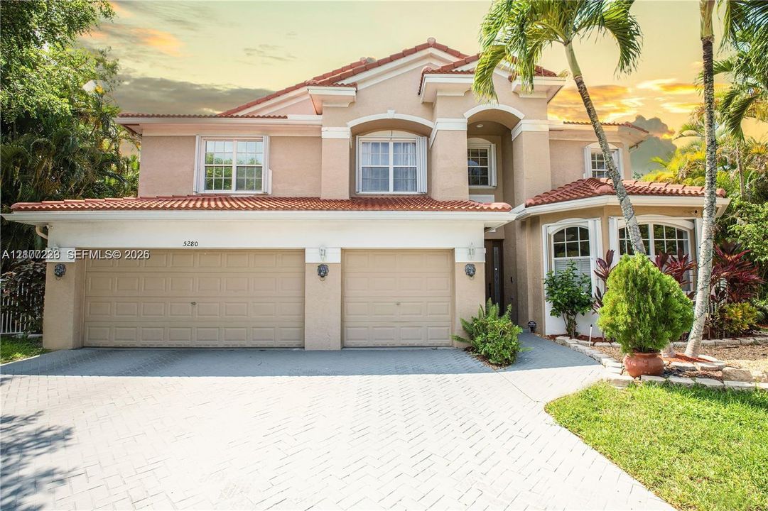 Two-story stucco exterior featuring a red tile roof, multi-pane windows, arched architectural accents, and a dual-bay garage