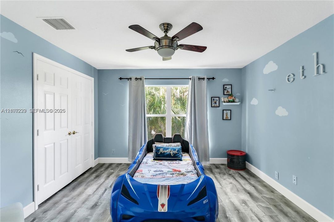 Bedroom featuring wood-finish flooring, a multi-blade ceiling fan with integrated lighting, and a double-door closet