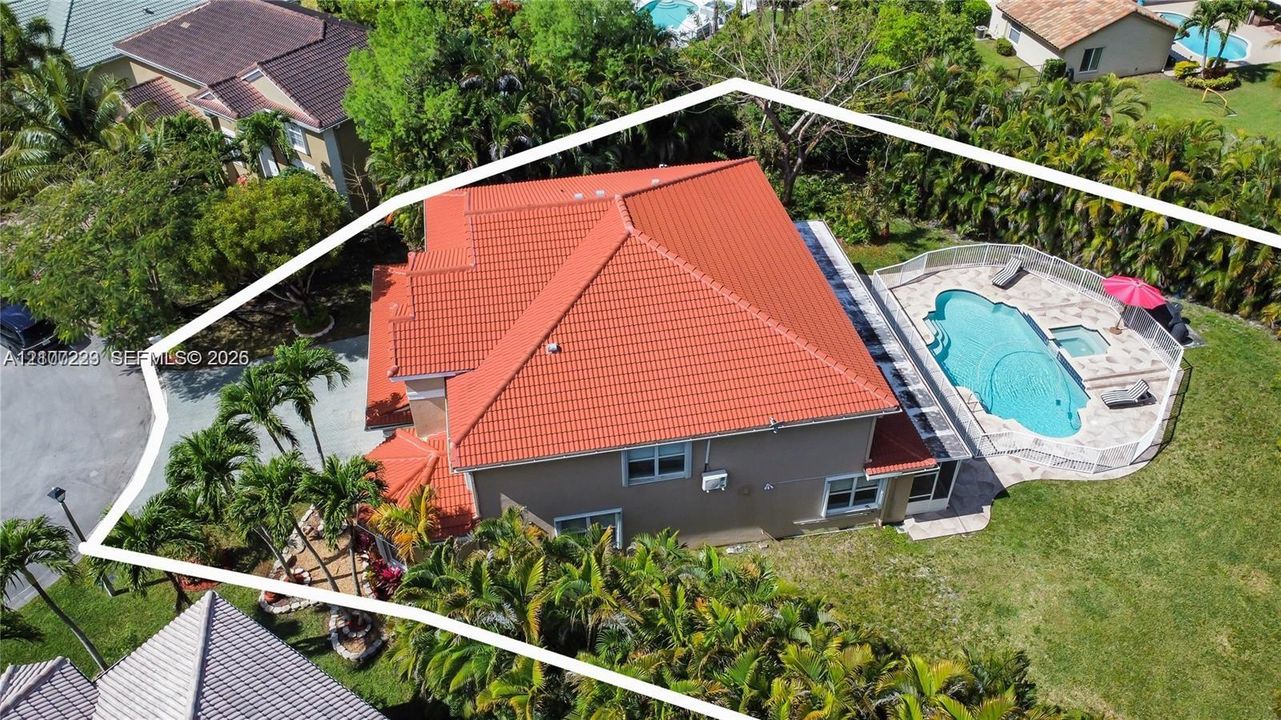 Aerial view of residential property featuring a tiled roof, an inground swimming pool with integrated spa, paved pool deck, and mature tropical landscaping