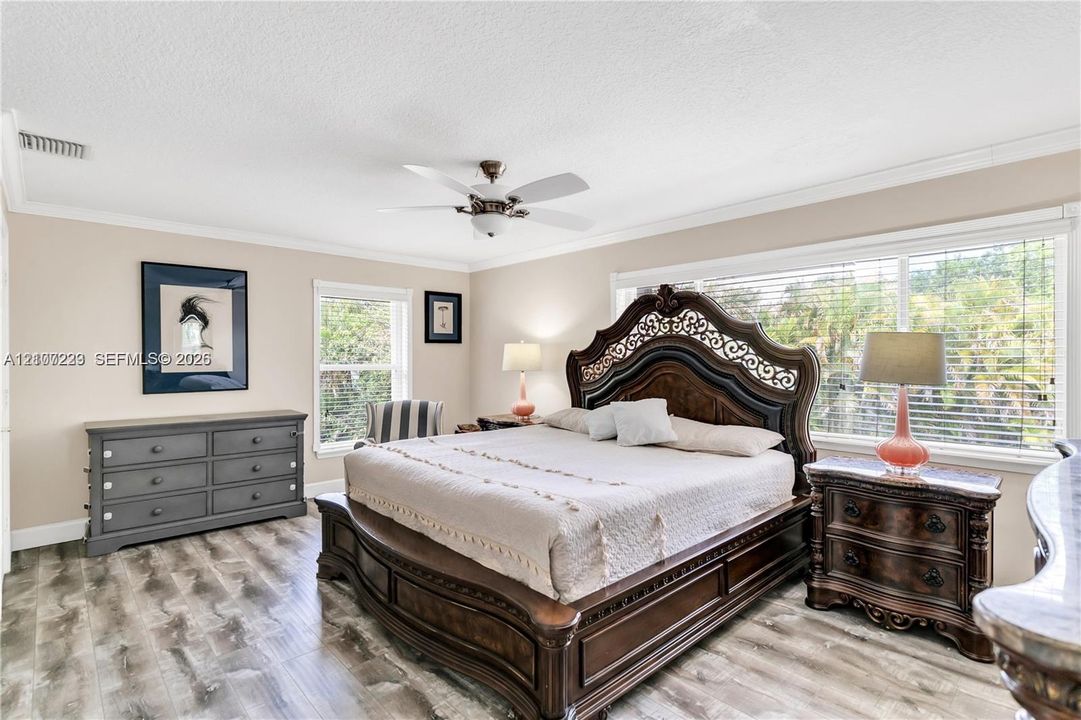 Bedroom featuring wood-finish flooring, crown molding, a ceiling fan with integrated lighting, and large windows with horizontal blinds