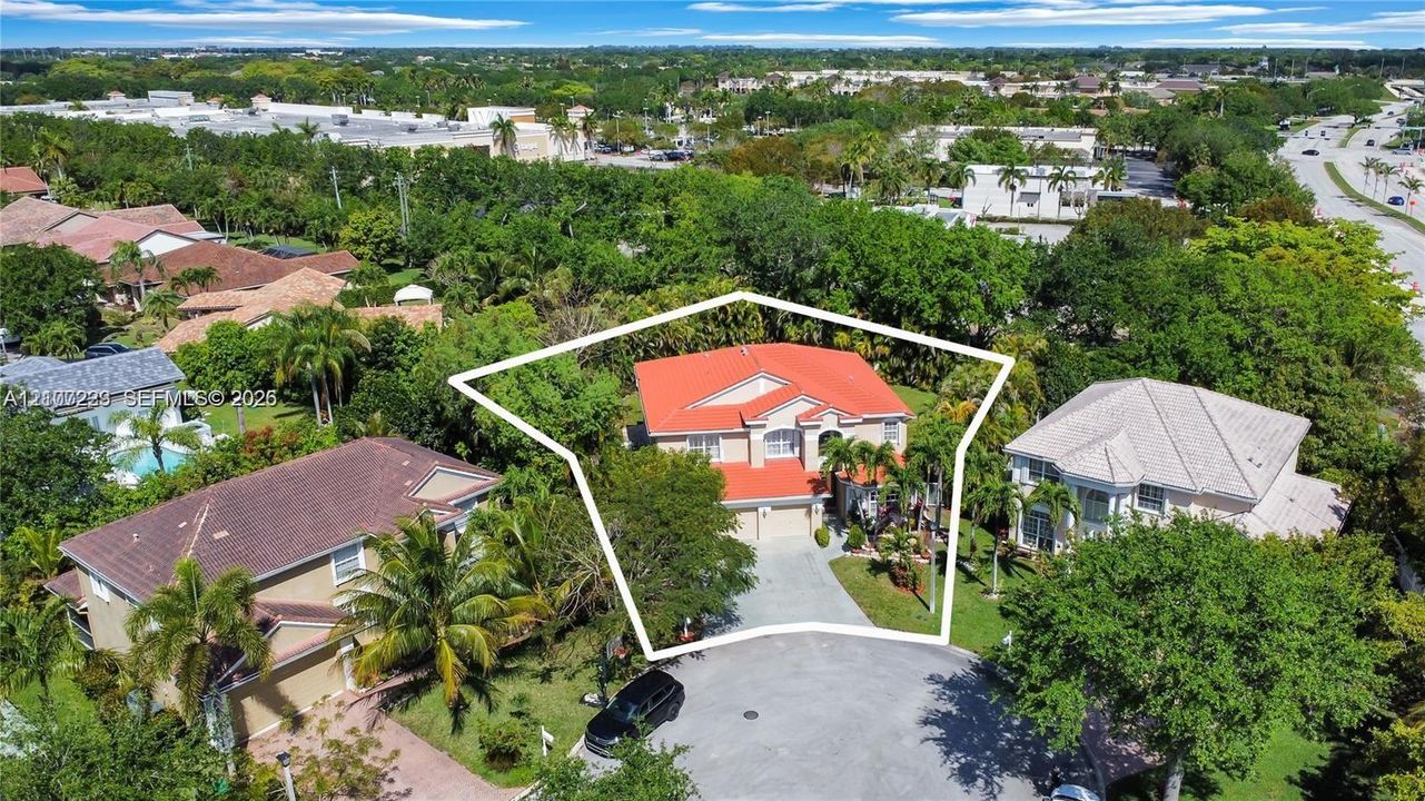 Two-story residence featuring a terracotta-tiled roof, light-toned exterior finish, multi-car garage, concrete driveway, and established perimeter vegetation