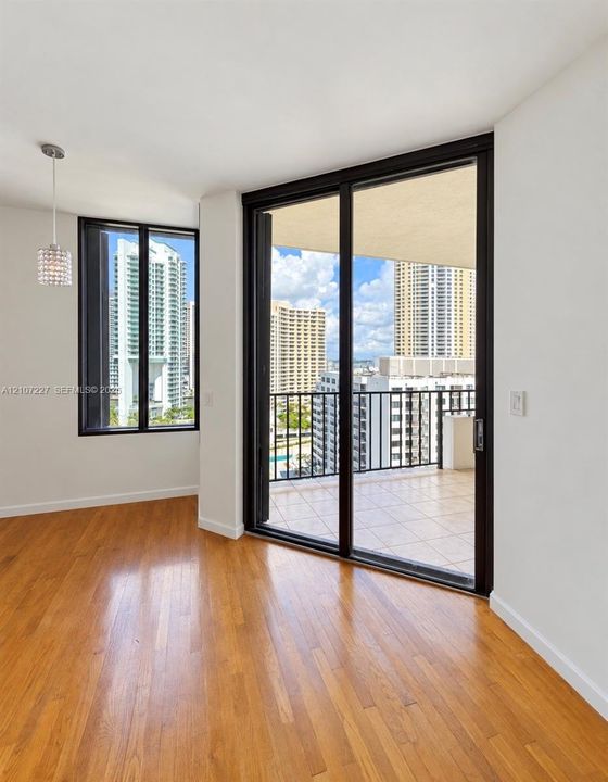 Wood-finish flooring, floor-to-ceiling glass sliding doors, private balcony with tile surfacing, and a crystal pendant light fixture