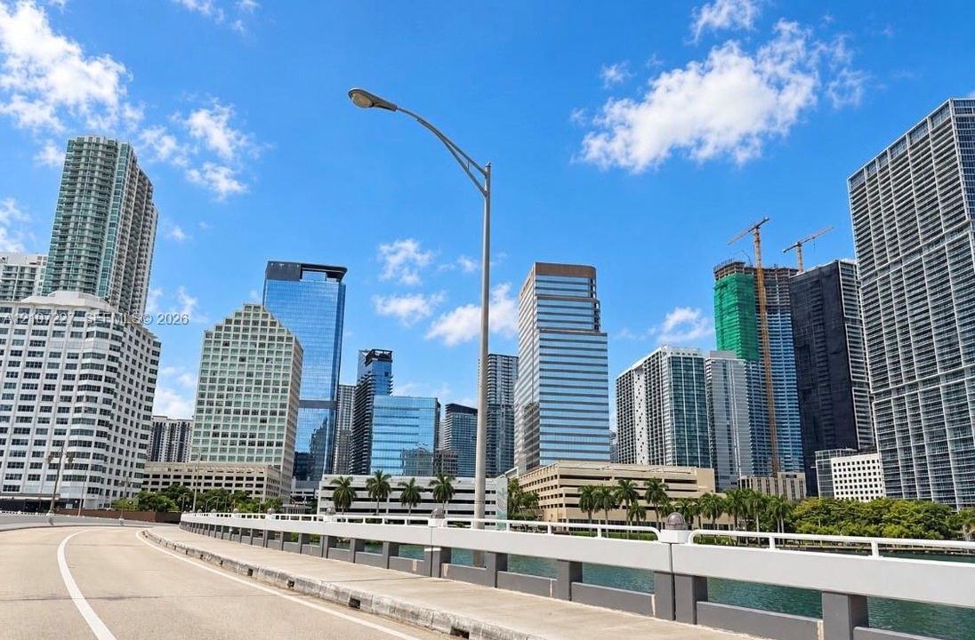 Urban landscape featuring a collection of high-rise commercial and residential towers, paved thoroughfare, and mature palm trees along the waterfront