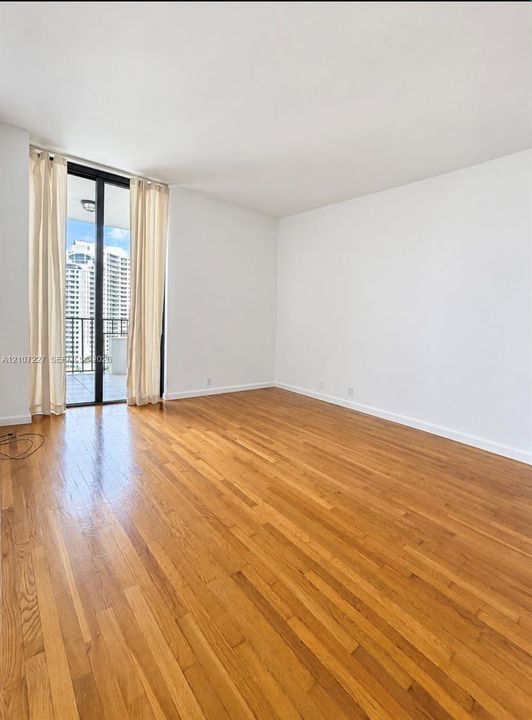 Interior living space featuring wood-finish flooring, neutral walls, and a glass-paneled door opening to a private balcony