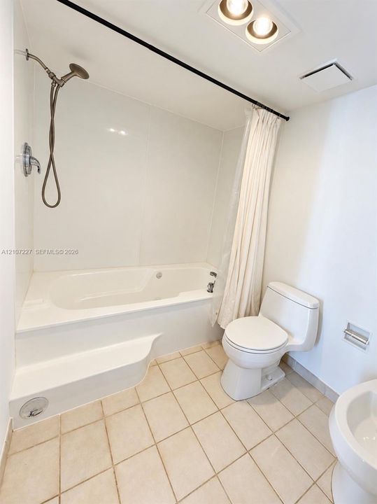 Bathroom featuring a deep soaking tub with an integrated step, an adjustable-height handheld showerhead, a seamless tub surround, and neutral tile flooring