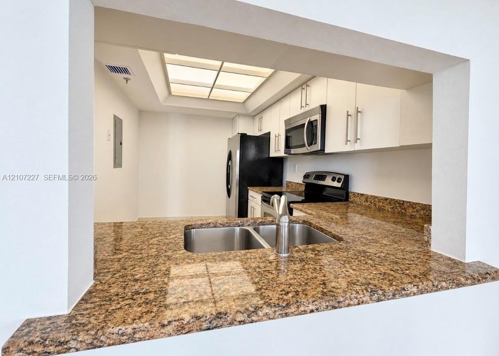 Kitchen featuring stone-finish countertops, stainless steel dual-basin undermount sink, built-in cabinetry with metallic pulls, stainless steel microwave, and recessed lighting