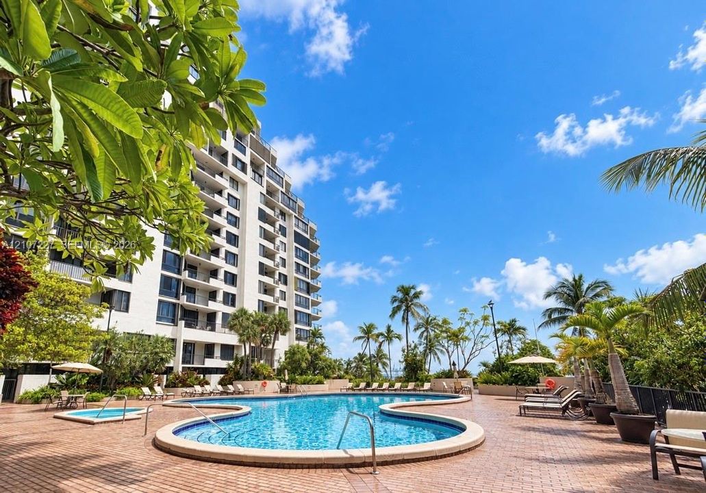 Curved swimming pool and spa surrounded by a brick-paver deck, mature palm trees, and professional landscaping