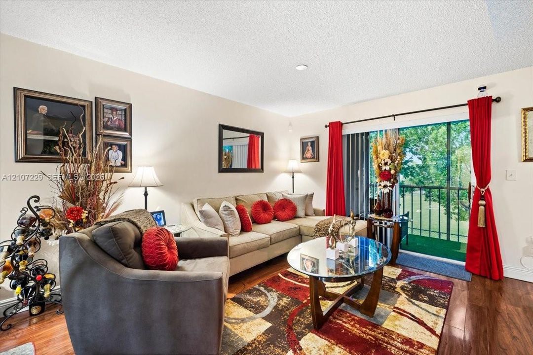 Living area featuring wood-finish flooring, recessed ceiling lighting, and a sliding glass door providing external access to a railed balcony