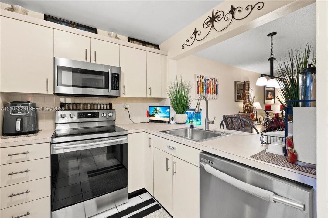 Kitchen featuring cream-colored cabinetry, stainless steel appliances, neutral countertops, a stainless steel undermount sink with a gooseneck faucet, and tile flooring