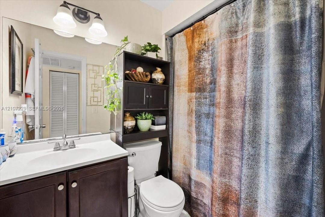 Bathroom featuring a dark wood-finish vanity, integrated countertop with sink, chrome faucet, wall-spanning mirror, and three-light vanity fixture