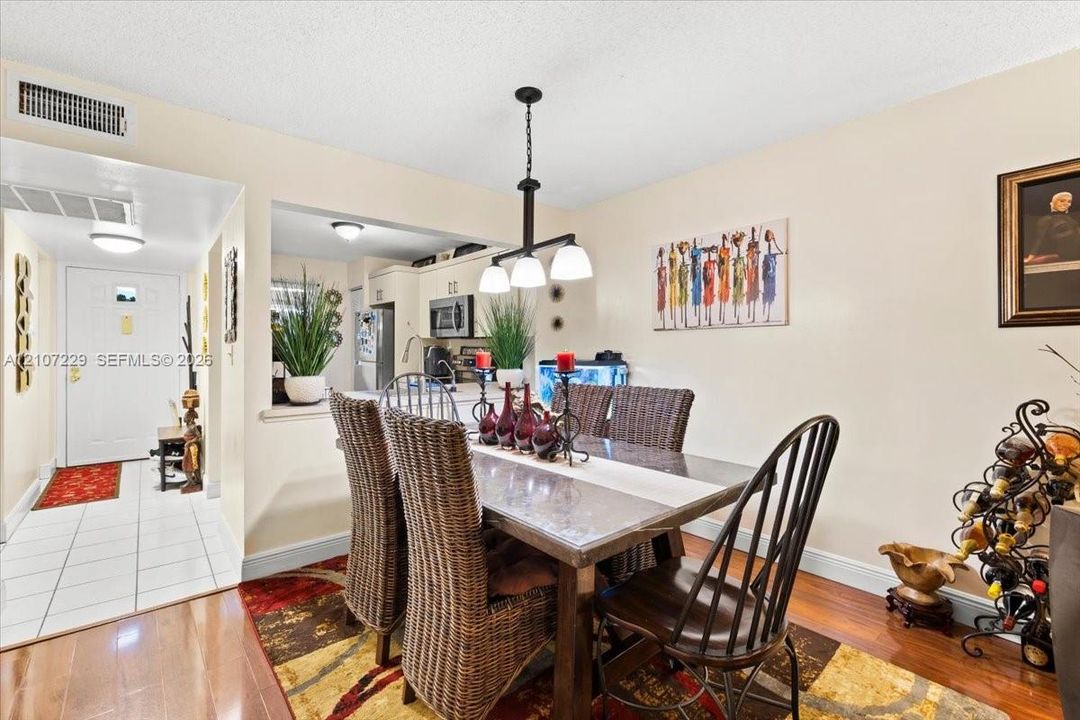 Dining area featuring wood-finish flooring, a three-light pendant fixture, and a pass-through opening to the kitchen