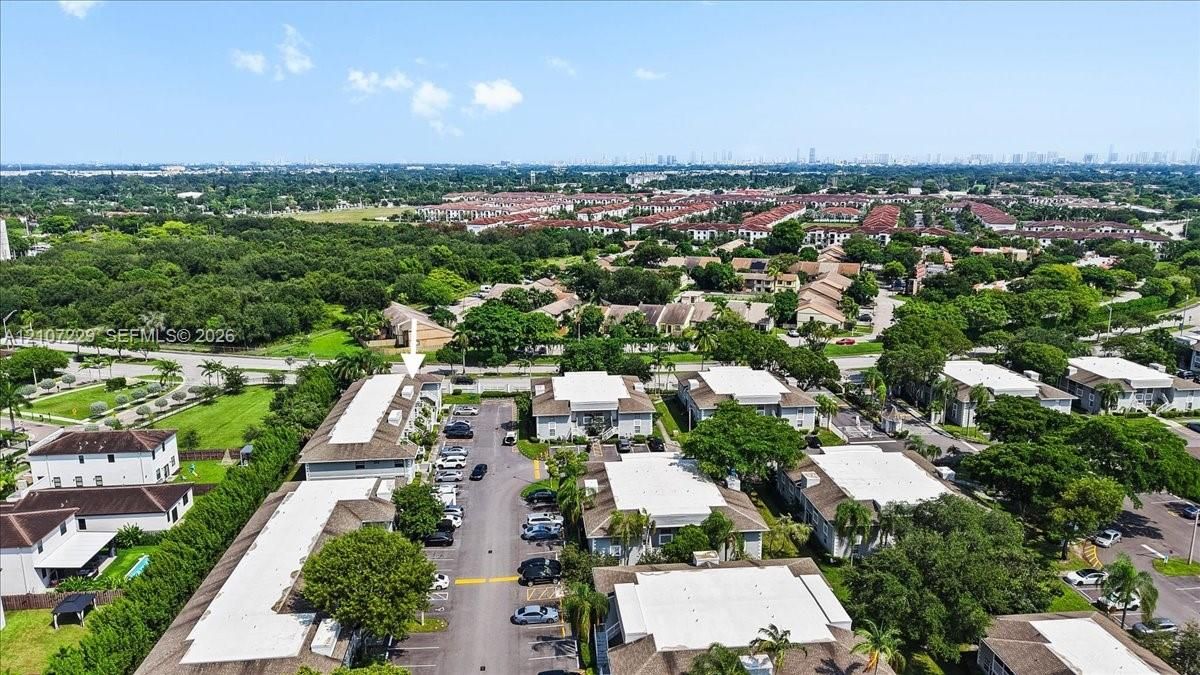 Aerial perspective of multi-family complex featuring white flat roofs, asphalt surface parking, and mature tropical landscaping