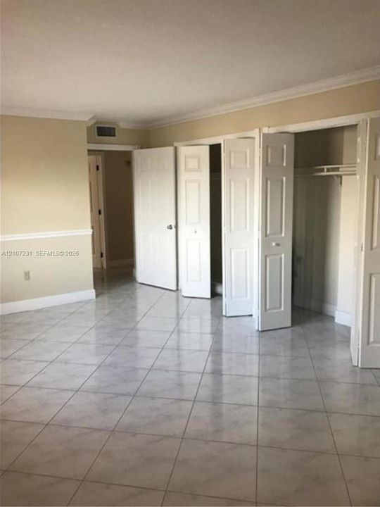 Interior space featuring light-toned tile flooring, chair rail molding, crown molding, and two sets of multi-panel closet doors
