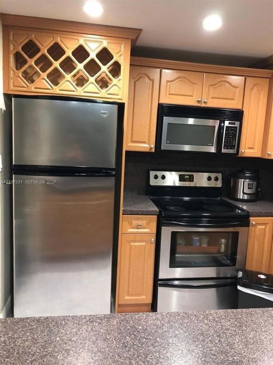 Kitchen featuring wood cabinetry, stainless steel appliances, built-in wine rack, and stone-finish countertops