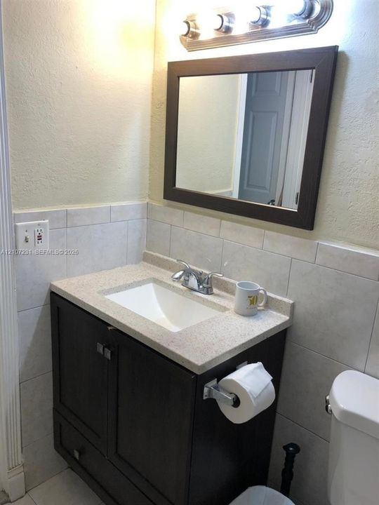 Dark wood vanity featuring a stone-composite countertop, undermount sink, ceramic tile backsplash, and a framed wall mirror
