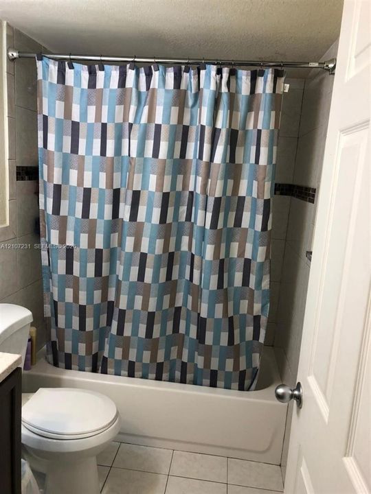 Full bathroom featuring tiled shower walls with a decorative accent border, a white porcelain tub, a white commode, and light-toned floor tiles