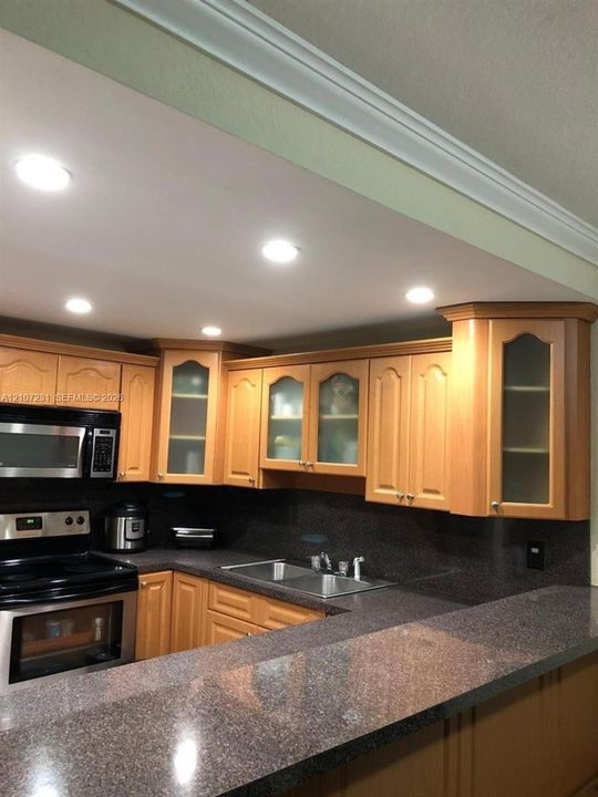 Kitchen featuring natural wood cabinetry with glass-front display panels, stone-finish countertops, stainless steel appliances, and recessed ceiling lighting