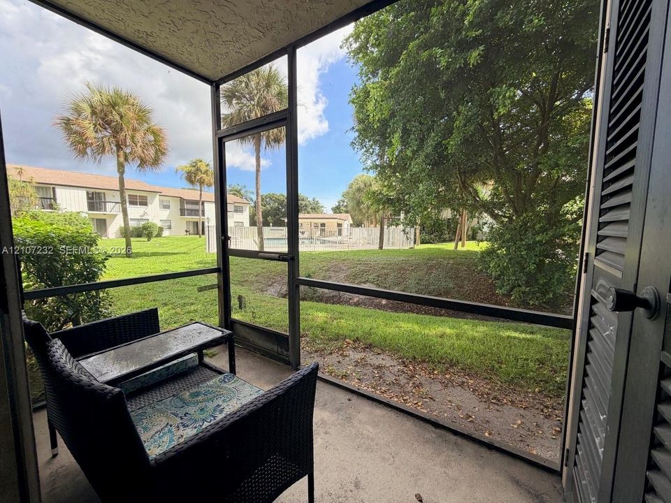Screened-in patio with concrete flooring, louvered exterior door, and metal framing, overlooking landscaped grounds with mature palm trees