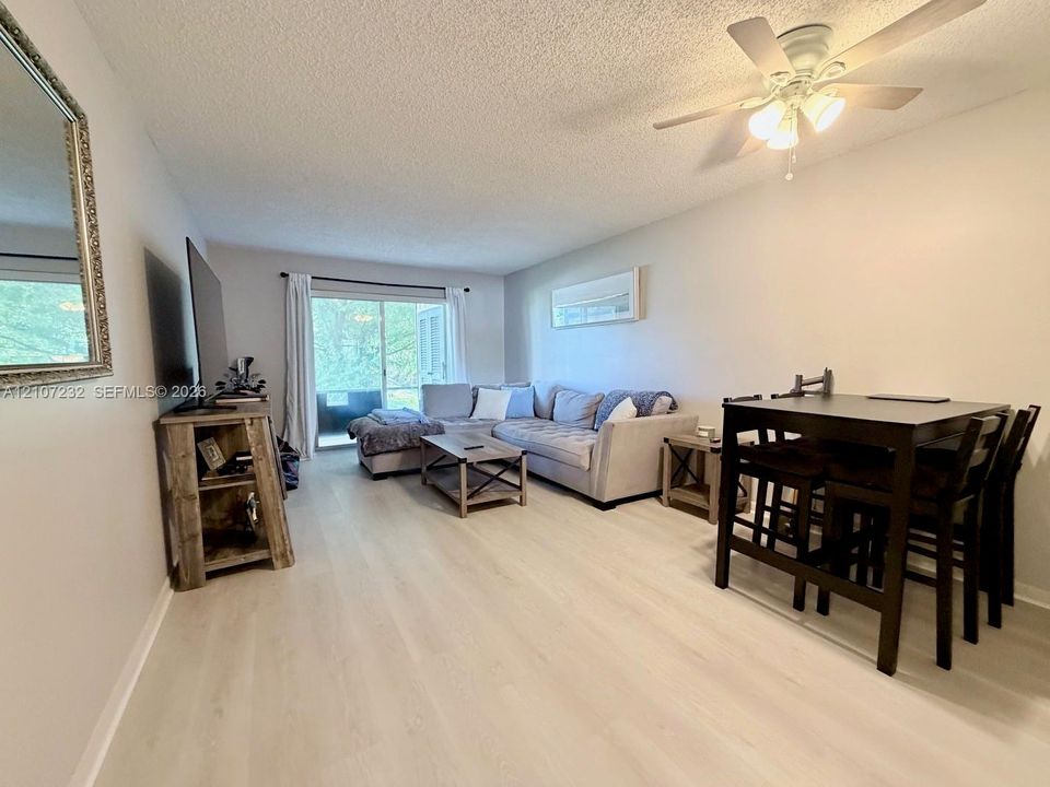 Open-concept living space featuring wood-finish flooring, a ceiling fan with integrated lighting, and a sliding glass door