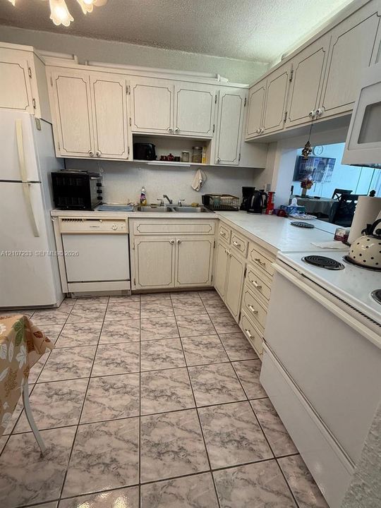 Kitchen featuring white cabinetry, solid-surface countertops, dual-basin stainless steel sink, and ceramic tile flooring