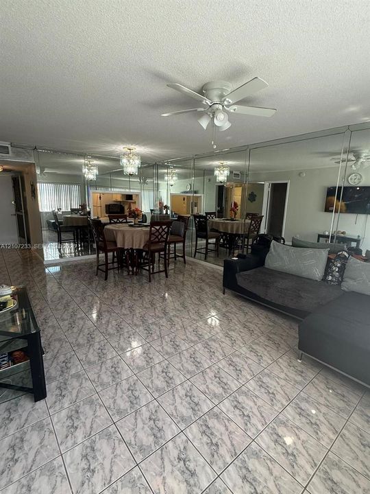 Spacious room featuring floor-to-ceiling mirrored walls, patterned tile flooring, a multi-blade ceiling fan, and a built-in crystal-style chandelier