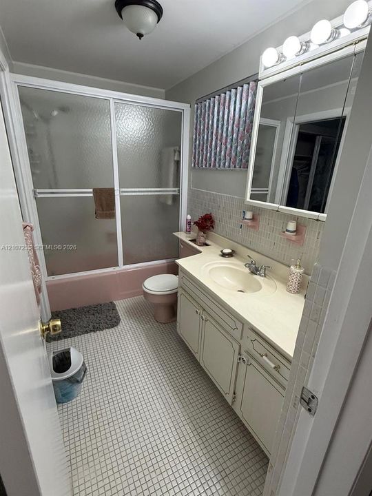 Bathroom featuring a vanity with integrated sink, glass-enclosed shower and tub combination, mirrored medicine cabinet, and tile flooring