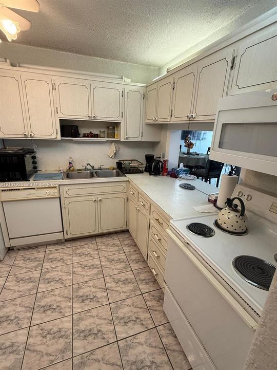 Kitchen featuring solid-surface countertops, white cabinetry with recessed-panel doors, a dual-basin sink, an over-the-range microwave, and ceramic tile flooring