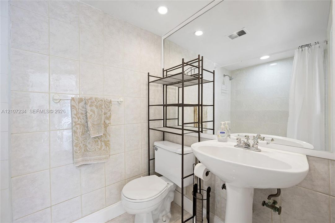Bathroom featuring full-wall tile surround, pedestal sink with chrome-finish faucet, and oversized wall-mounted mirror