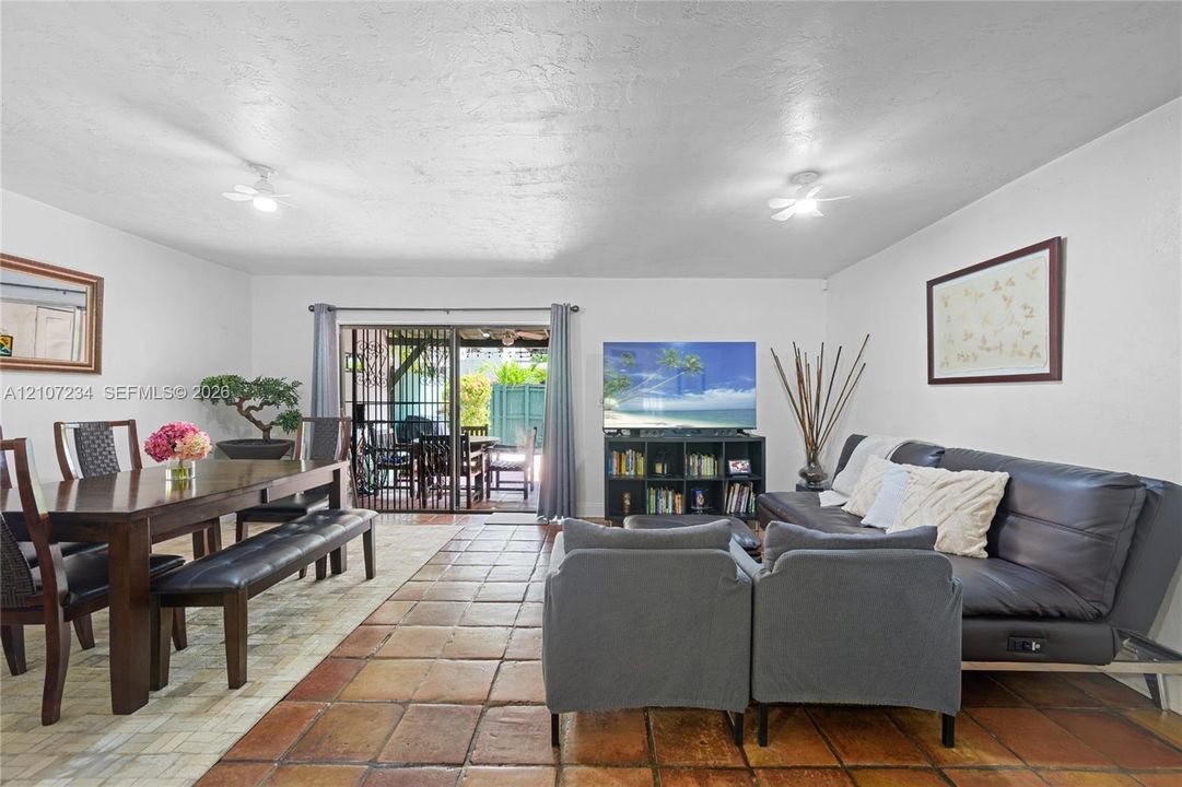 Open-concept living space featuring large-format ceramic tile flooring, dual ceiling-mounted lighting fixtures, and sliding glass doors providing access to the rear exterior