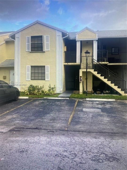 Two-story multi-family exterior featuring light-toned stucco siding, louvered shutters, metal railings, and a dedicated staircase