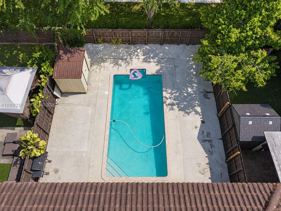 In-ground rectangular swimming pool with concrete patio surround, enclosed by a wood privacy fence and featuring two detached storage structures