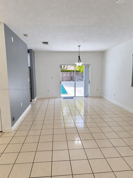 Neutral-tone interior featuring ceramic tile flooring, a dark-toned accent wall, a tiered hanging light fixture, and sliding glass doors opening to an exterior pool area