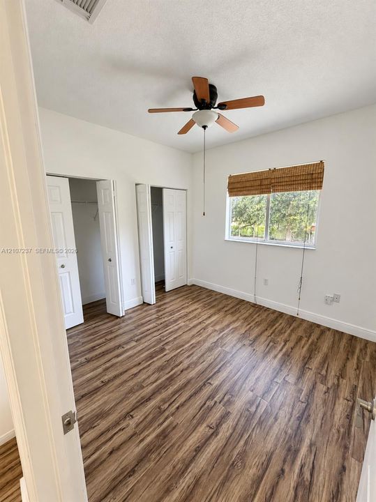 Wood-finish flooring, dual reach-in closets with panel doors, and a ceiling fan with integrated lighting