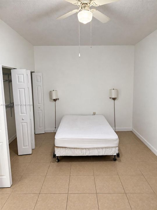 Room featuring neutral tile flooring, bi-fold closet doors, and a ceiling-mounted light fixture with a fan