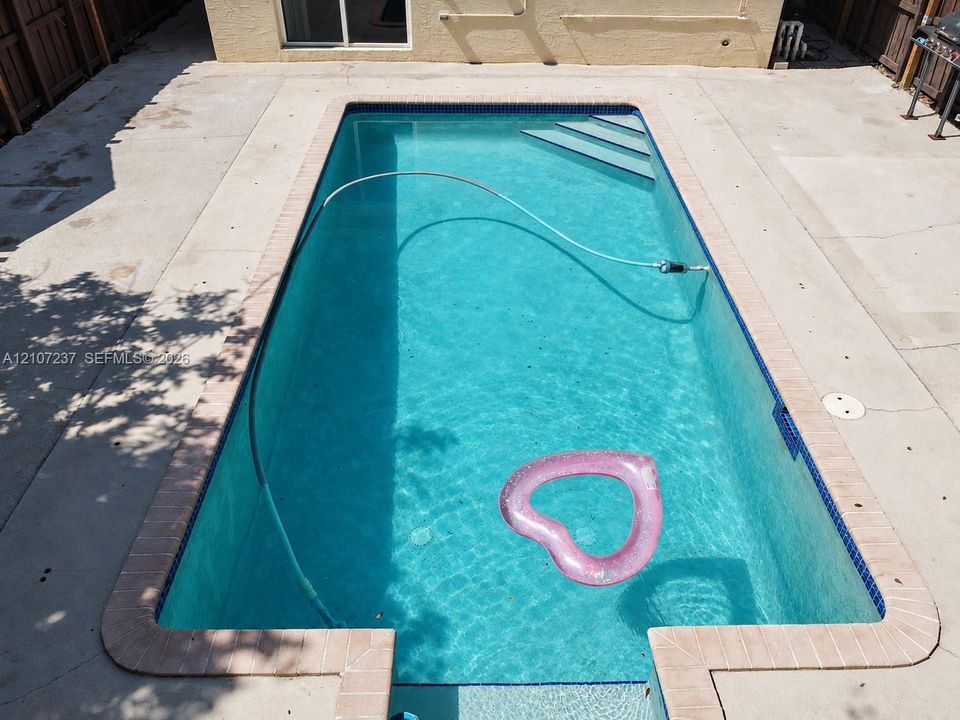 Rectangular in-ground swimming pool featuring a brick-tiled coping, built-in entry steps, and a concrete patio surround