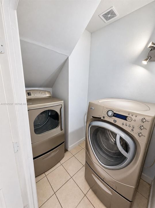 Laundry space featuring large-format ceramic tile flooring and wall-mounted metal task lighting