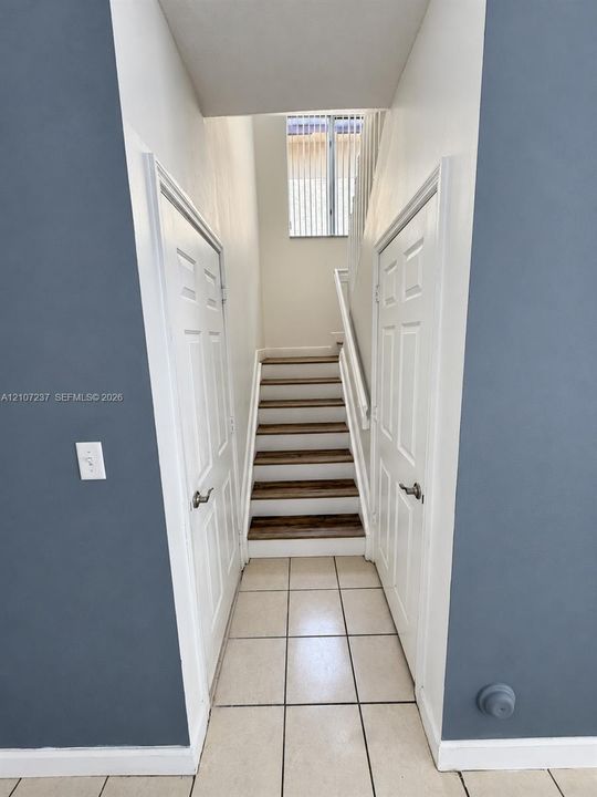 Staircase featuring wood-finish treads, white risers, and a matching handrail, flanked by two six-panel doors and finished with ceramic tile flooring