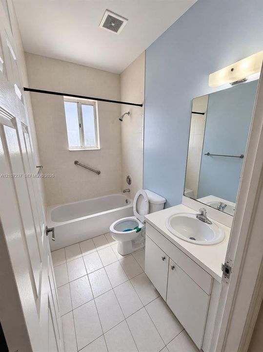 Bathroom featuring a white porcelain tub with an integrated shower, vanity cabinet with an inset sink, solid-surface countertop, and large wall-mounted mirror