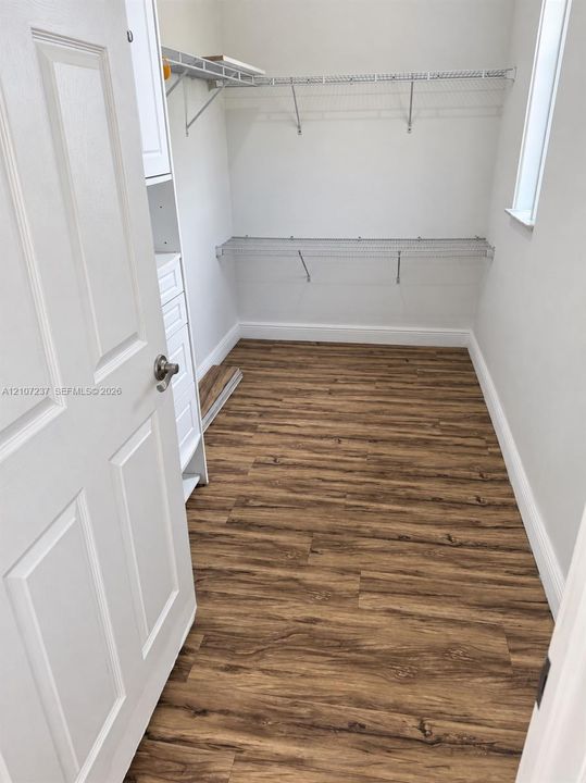 Storage space featuring wood-finish flooring, white built-in cabinetry with drawers, and multi-tier wire shelving