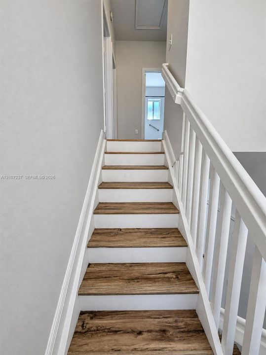 Staircase featuring wood-finish treads, white risers, and a white baluster railing