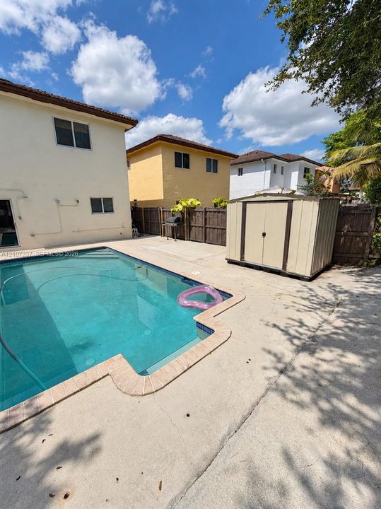 In-ground swimming pool with stone coping, expansive concrete patio, and detached storage structure, enclosed by a wood privacy fence