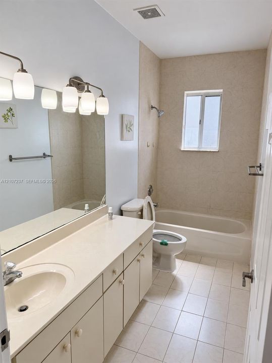 Bathroom featuring a large vanity with integrated countertop, wall-to-wall mirror, multi-light fixture, tile flooring, and a tiled tub-shower combination