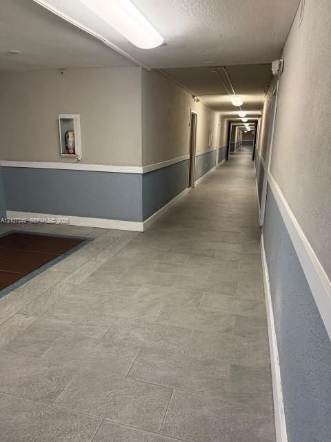 Hallway featuring light-toned stone-finish flooring, two-tone painted walls with chair rail trim, and flush-mount overhead lighting