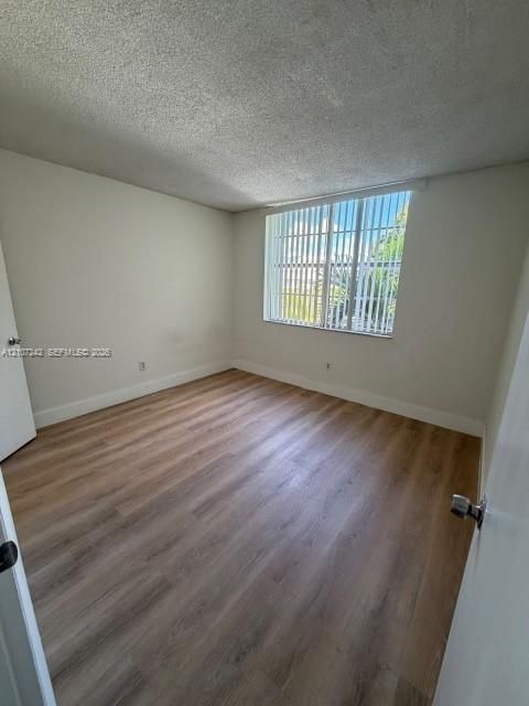 Room featuring wood-finish flooring, a large window, and vertical window blinds