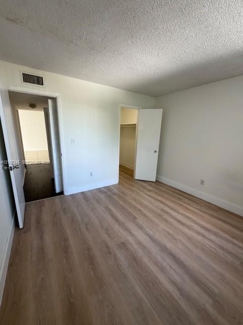 Room featuring wood-finish flooring, white walls, textured ceiling, and a built-in closet with a hinged door