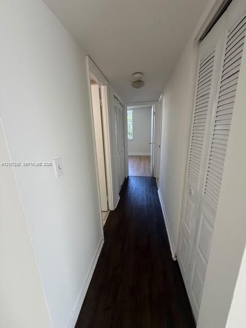 Hallway featuring dark wood-finish flooring, white walls, and built-in closet storage with louvered doors