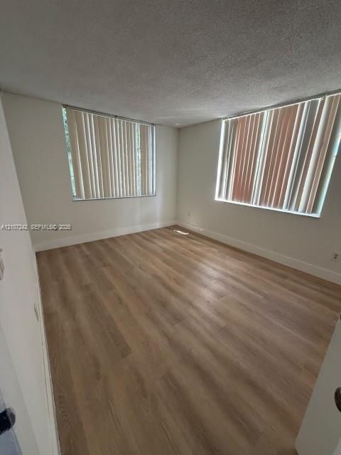 Interior room featuring wood-finish flooring, neutral wall tones, and two large windows with vertical blinds