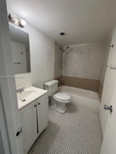 Bathroom featuring a white vanity cabinet with an integrated sink, a rectangular wall-mounted mirror, a two-piece toilet, and a bathtub with a tiled shower surround
